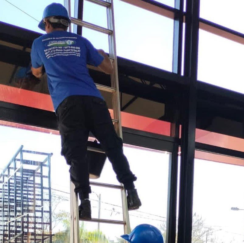 Técnico de Brillo Total realizando limpieza de fachada de vidrio en altura, sobre plataforma elevadora